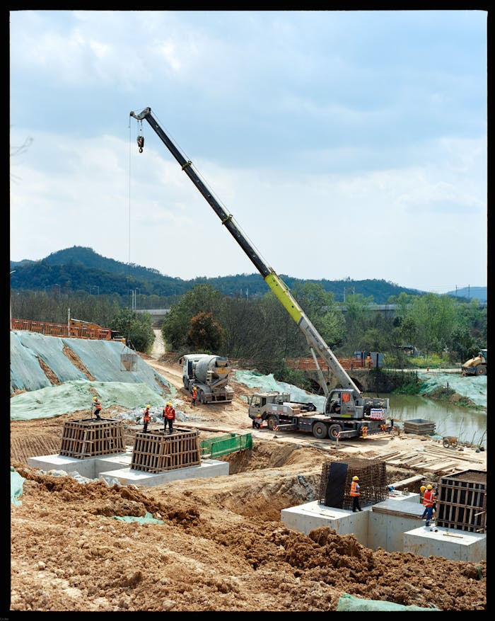 Active construction site featuring crane operation and workers amid a natural landscape.